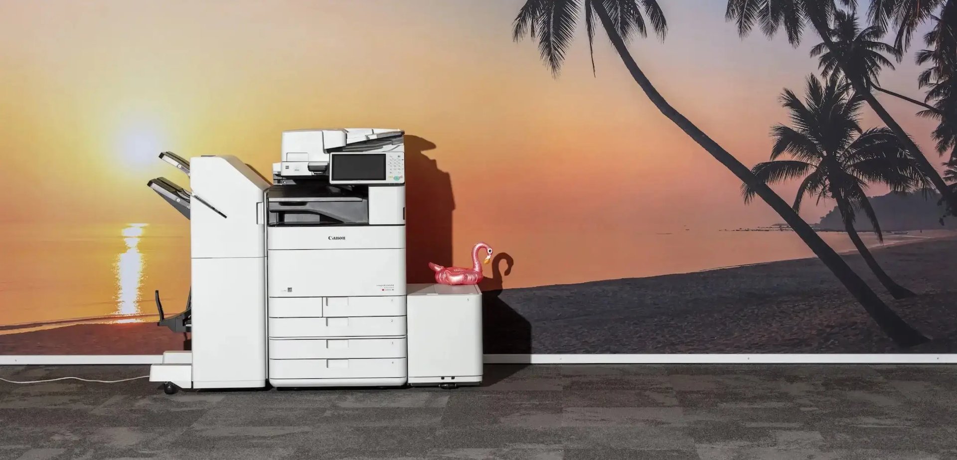 Ein Drucker von Canon steht vor einer Tapete, die einen Sonnenuntergang zeigt.